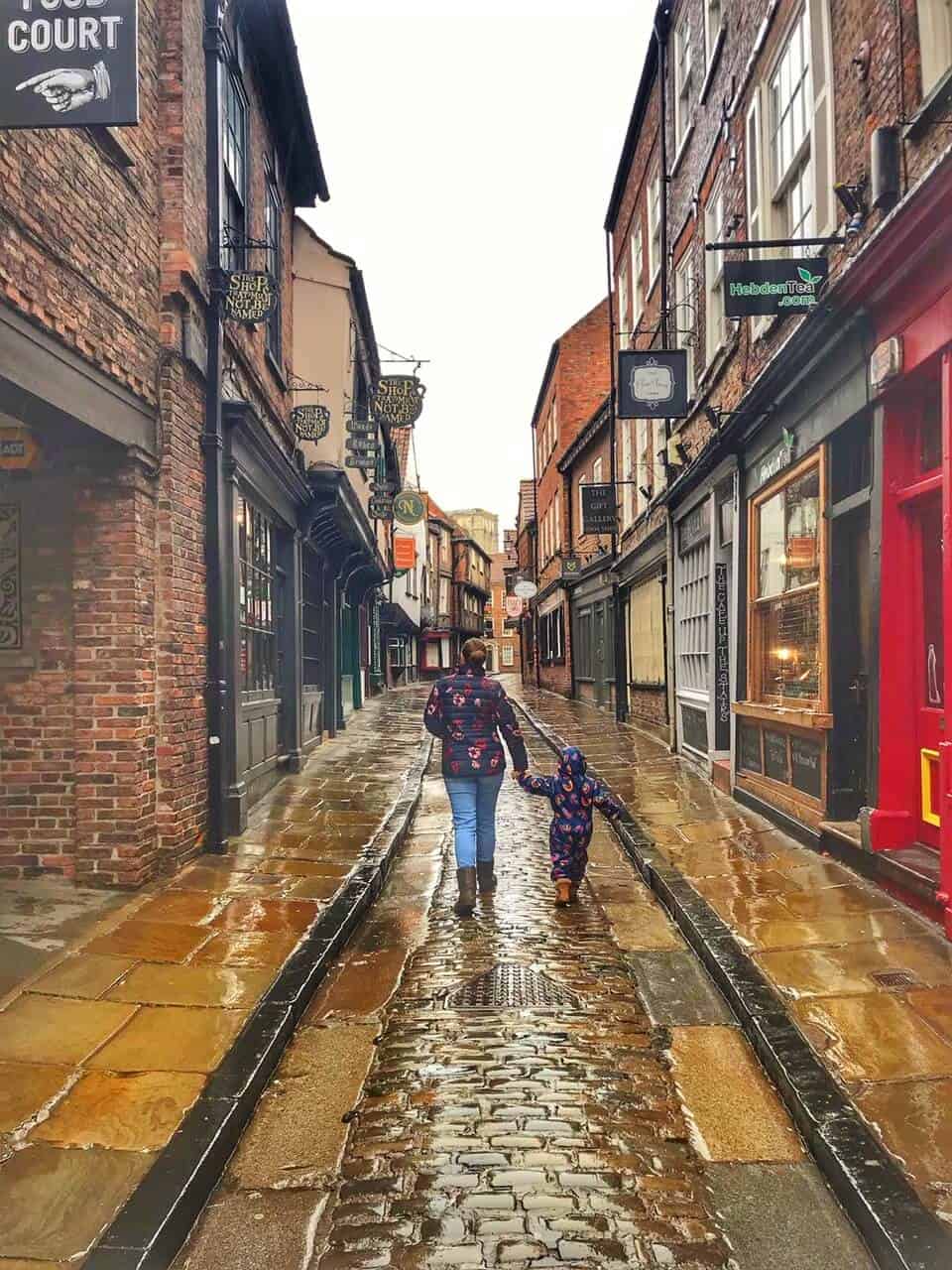 Woman holding a toddlers hand walking down the Shambles Street in York with no crowds after rain.