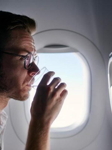 Man on plane drinking water - How to Stay Hydrated on a Plane
