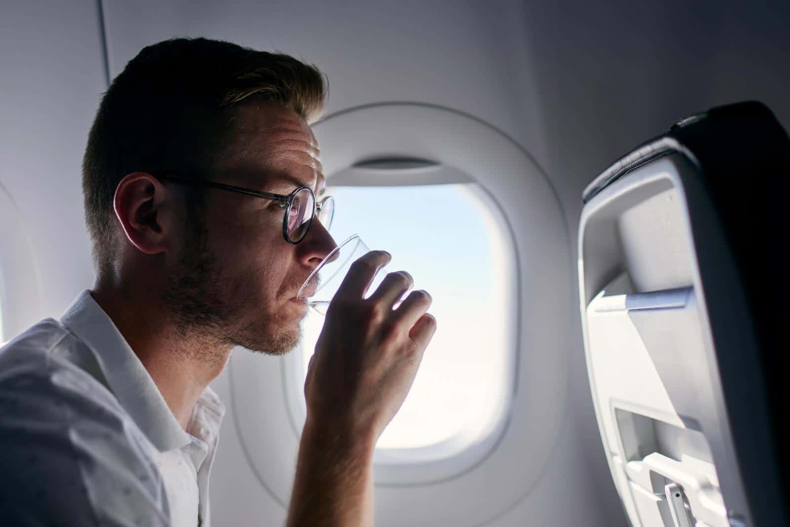 Man on plane drinking water - How to Stay Hydrated on a Plane